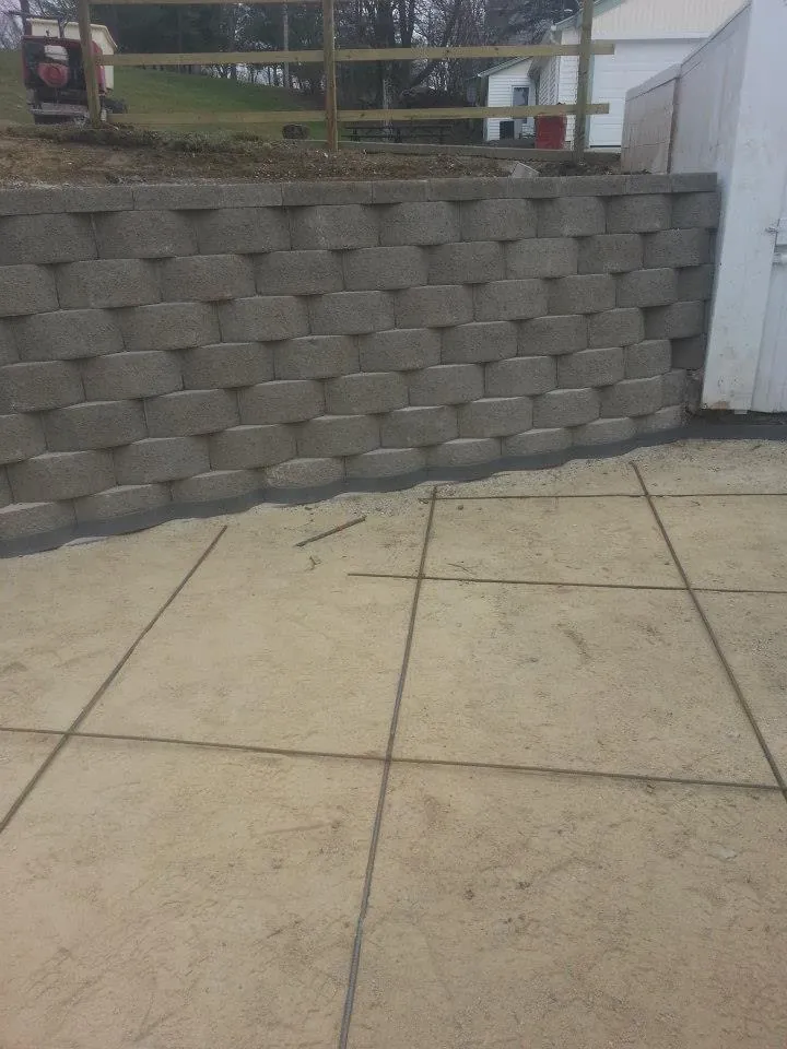 New block retaining wall above a concrete patio slab cut into squares with control joints