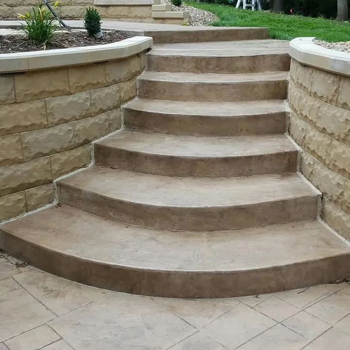 Wide curved stamped concrete steps climbing between two block retaining walls