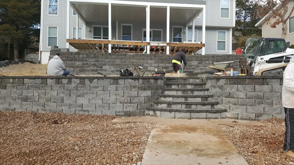 Tiered block retaining walls and steps being built by the S & M Concrete crew, with a skid steer on site
