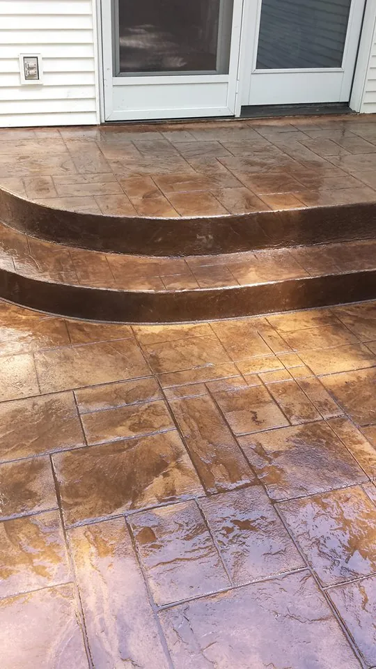 Curved stamped concrete entry steps with a brown stain leading to a back door