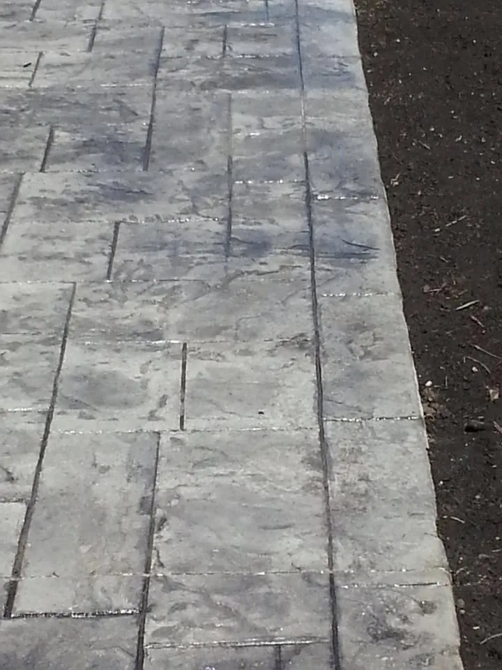 Gray stamped concrete walkway with a slate pattern next to a fresh dirt bed